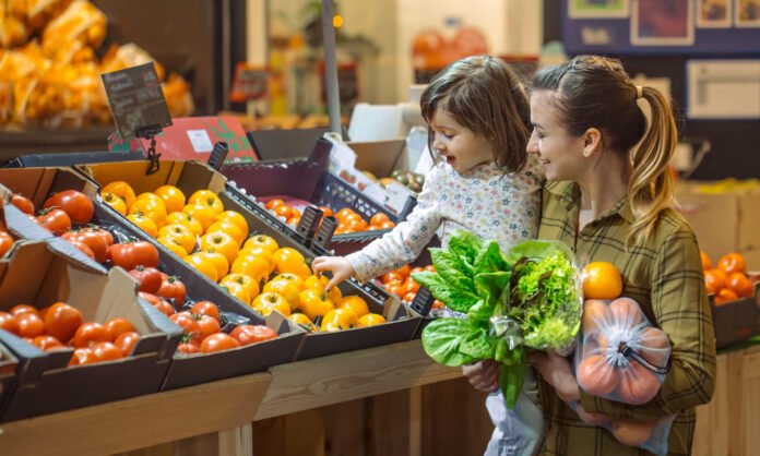 Family in the supermarket. Beautiful young mom and her little daughter smiling and buying food.