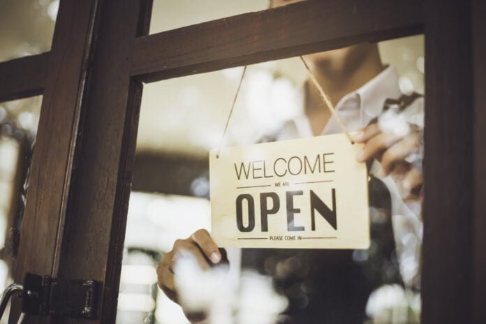 Store owner turning open sign broad through the door glass and ready to service.