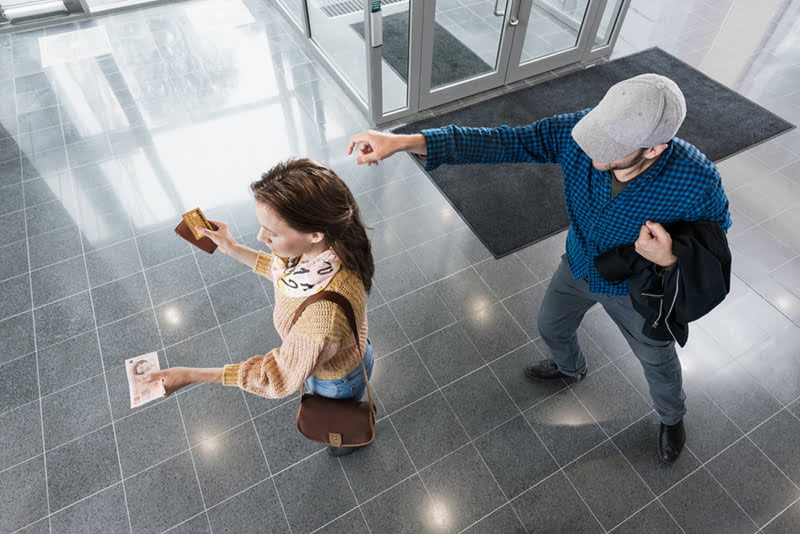 WOMAN HOLDING CASH AND A CREDIT CARD WITH A MAN BEHIND HER ATTEMPTING TO STEAL HER POSSESSIONS. PHOTO: AXIS COMMUNICATIONS