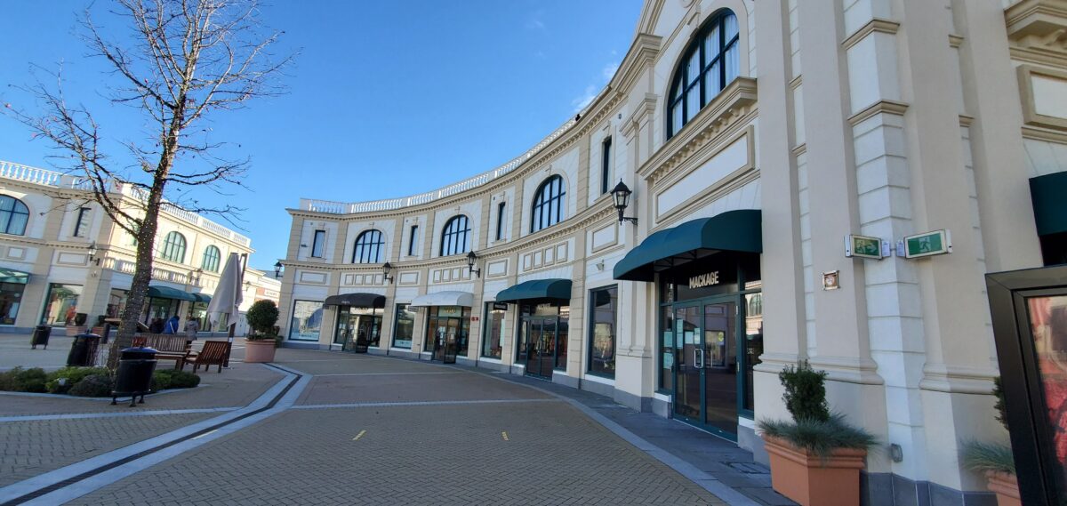Row of Retailers circling the SEI statue at McArthur Glen Vancouver, including Ports, Maje and Mackage
