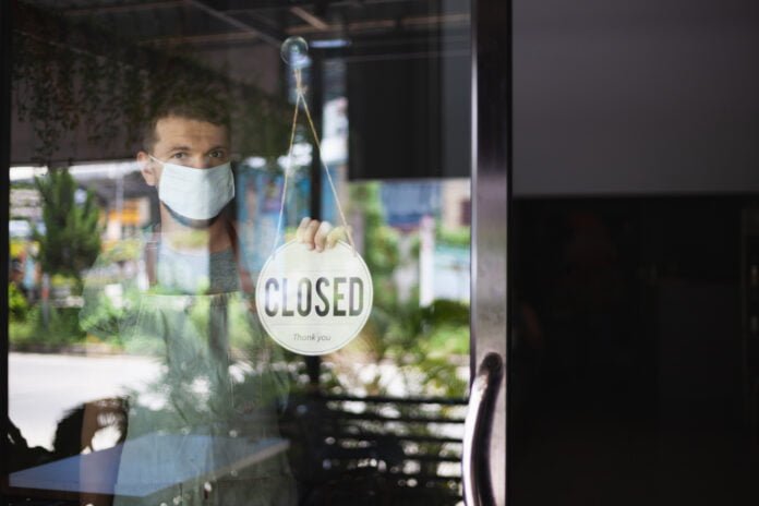 Chef wearing a mask hanging up sign closed on restaurant door. Chef wearing a mask hanging up sign closed on restaurant door.